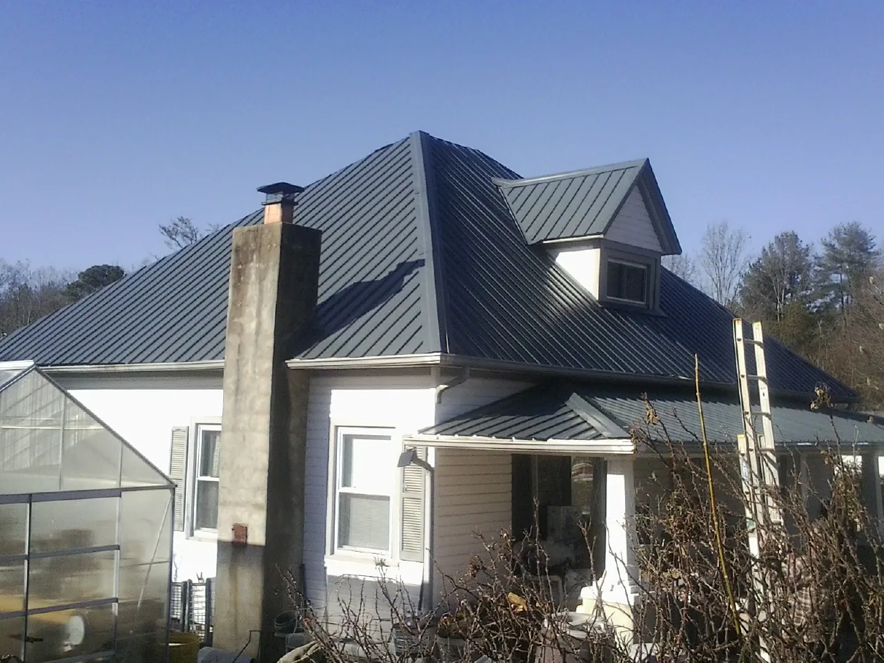 Dark blue standing seam metal roof on a white farmhouse with dormer in Barnes City