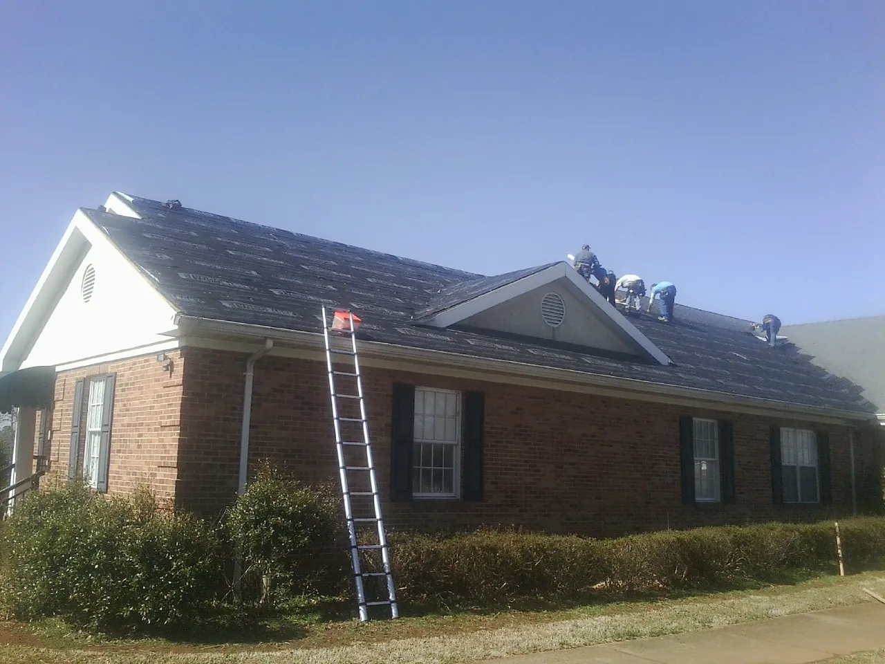 Crew tearing shingles off a brick ranch roof with a ladder set — Emergency Roof Repair work by our crew in Barnes City
