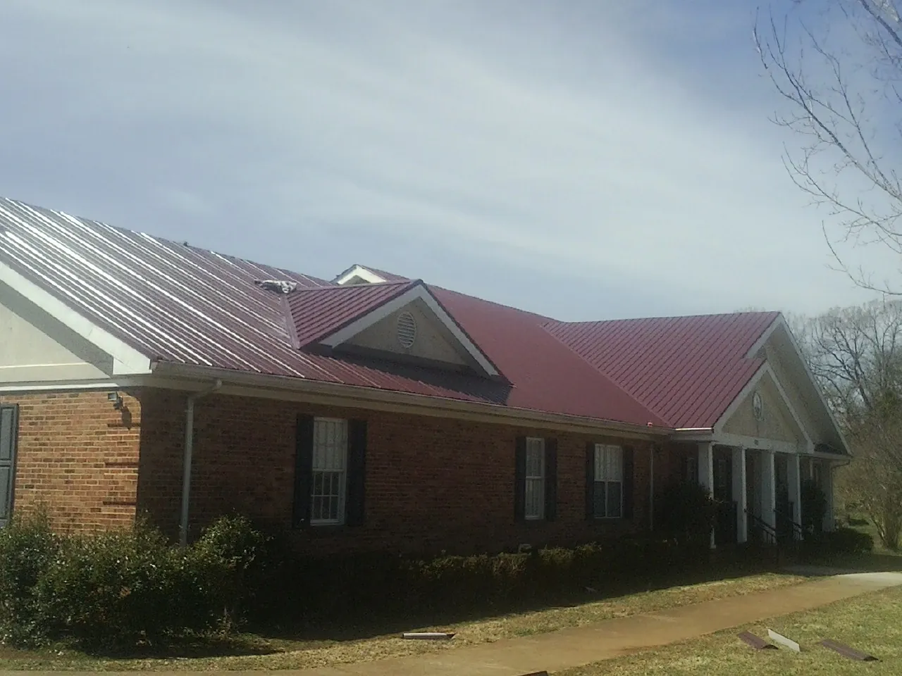 Red metal roof with gabled entries on a long brick building, from a Hail Damage Roof Repair job in Barnes City