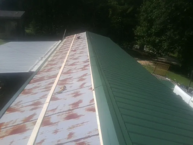 Old rusted panels beside newly installed green metal roofing — Wind Damage Roof Repair by Roofing Brothers in Barnes City