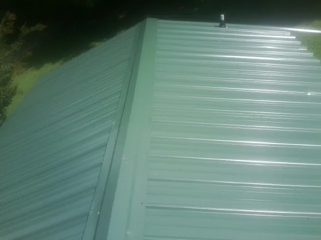 New green metal panels meeting at the ridge of a roof — Flat Roof Repair work by our crew in Barnes City