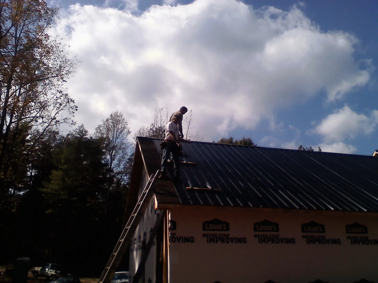 Roofer fastening dark metal panels high against a cloudy sky, from a Roof Inspection job in Barnes City
