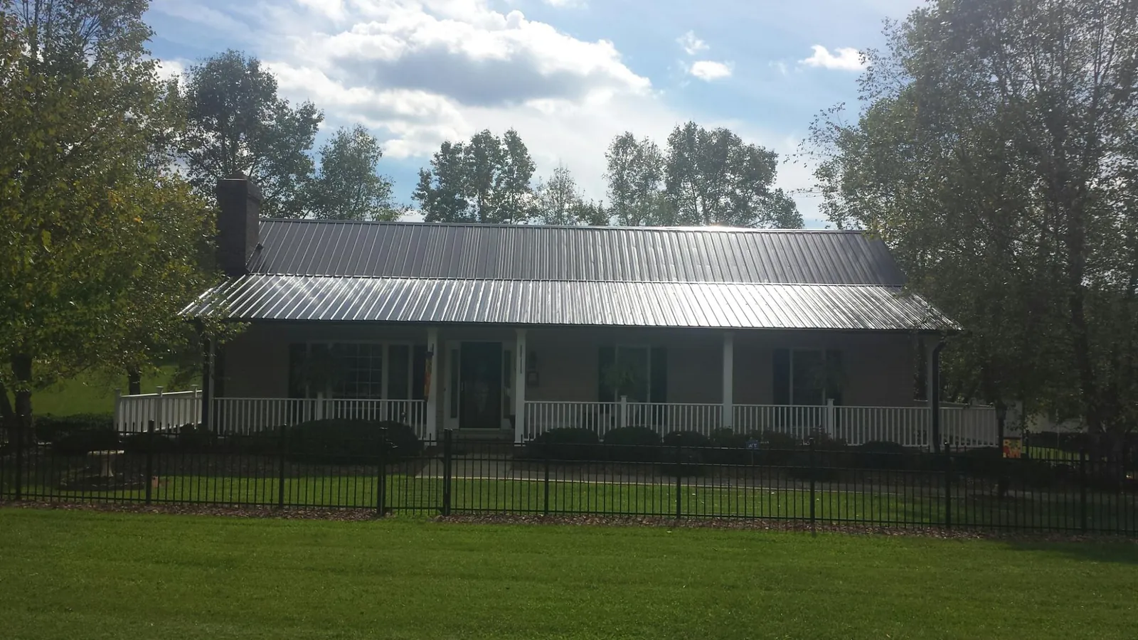 Gray metal roof on a brick ranch with a full width front porch — Gutter Guard Installation work by our crew in Barnes City