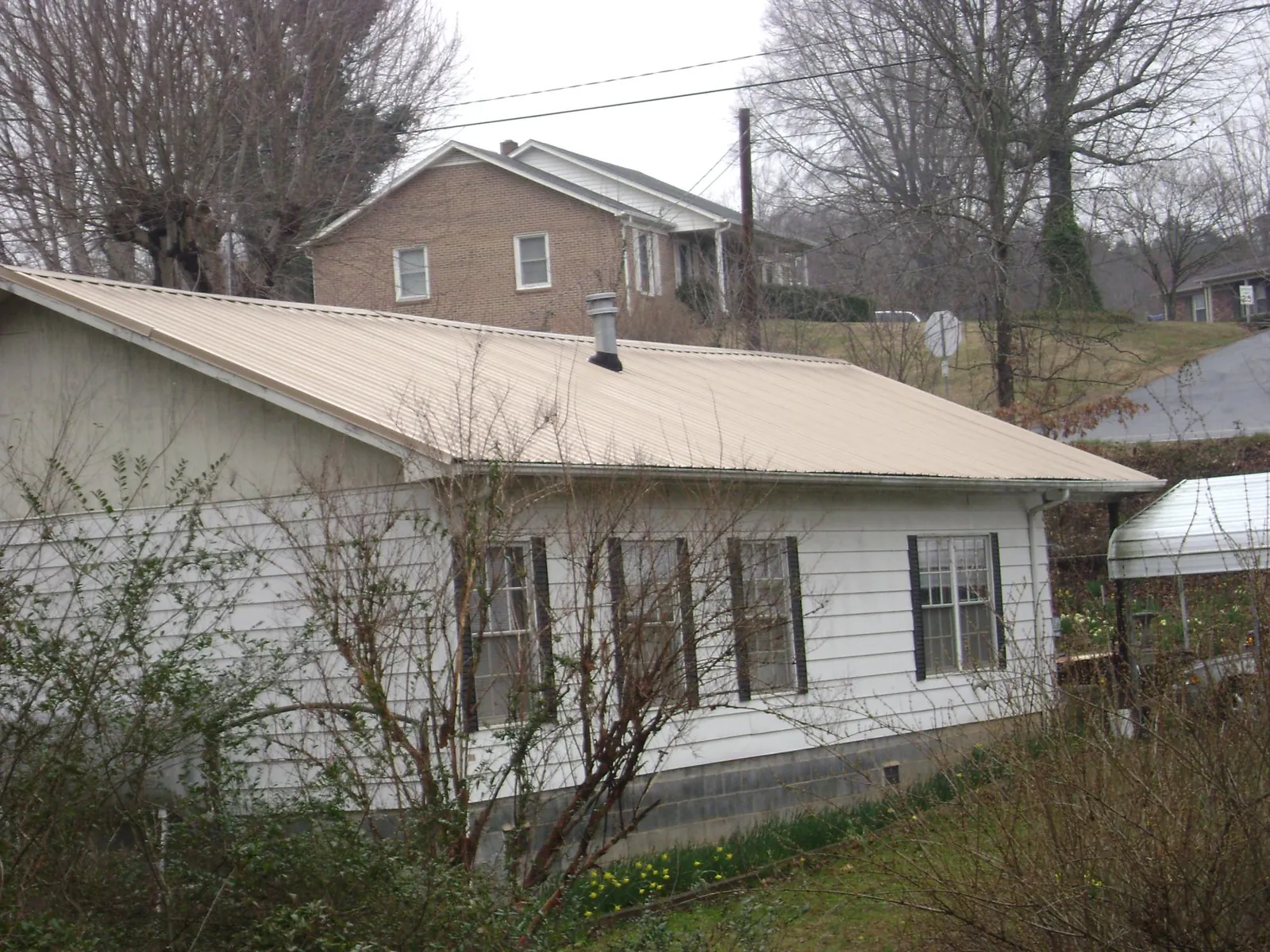 Tan metal roof on a white sided house set into a hillside — Commercial Roofing by Roofing Brothers in Barnes City