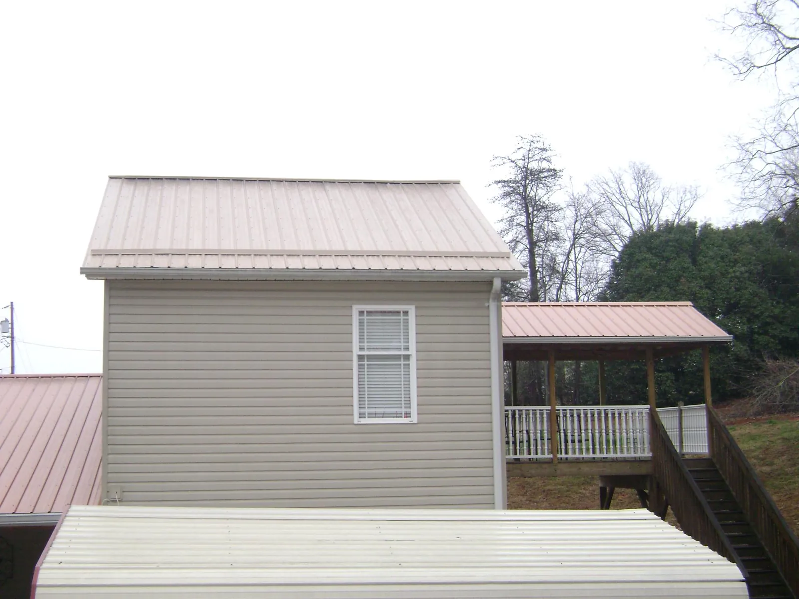 Tan metal roofs on a two story addition and attached porch, from a Roof Replacement job in Barnes City